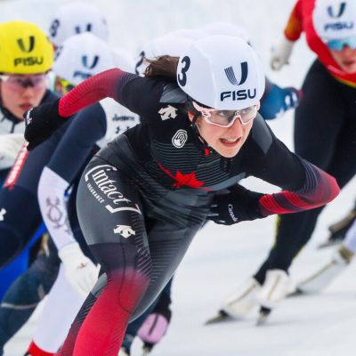 A line of women speed skaters skating fast and competing in a race in the 2023 FISU Games in Lake Placid.