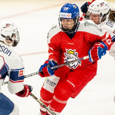 Three women hockey players battle for position and the puck on the ice in the 1980 Herb Brooks Arena.