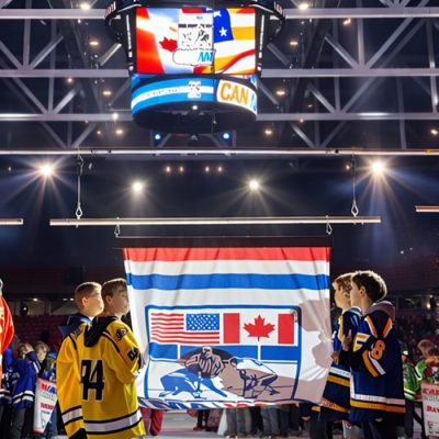 Opening ceremonies for a CAN/AM hockey tournament with the illuminated screen high above youth hockey players on the ice below in the 1980 Herb Brooks Arena.