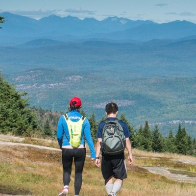 Two hikers high on Gore Mountain in the summer walking away from the camera toward the background view of the mountains.