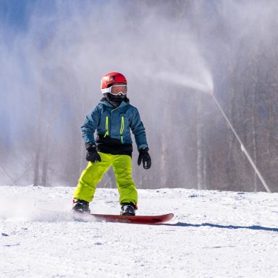 A young snowboarder slides down a snowy trail at Belleayre Mountain in the Catskills with a snowgun blowing fresh clean snow behind him.