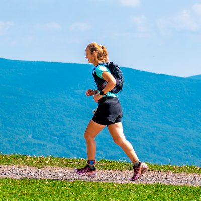 A woman with a small backpack runs across the top of Belleayre Mountain during the Climb It for Climate race with a beautiful view of the Catskills in the background.