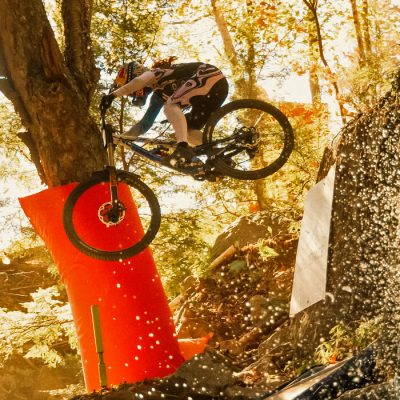 A rider in the Downhill World Cup event at Whiteface Mountain soars over a jump at a waterfall with the droplets glistening in the sun.