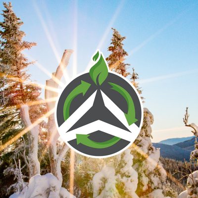 A winter scene on a mountaini top with blue sky behind snowy trees and the sun shinging behind the Olympic Authority sustainability logo in green and white.